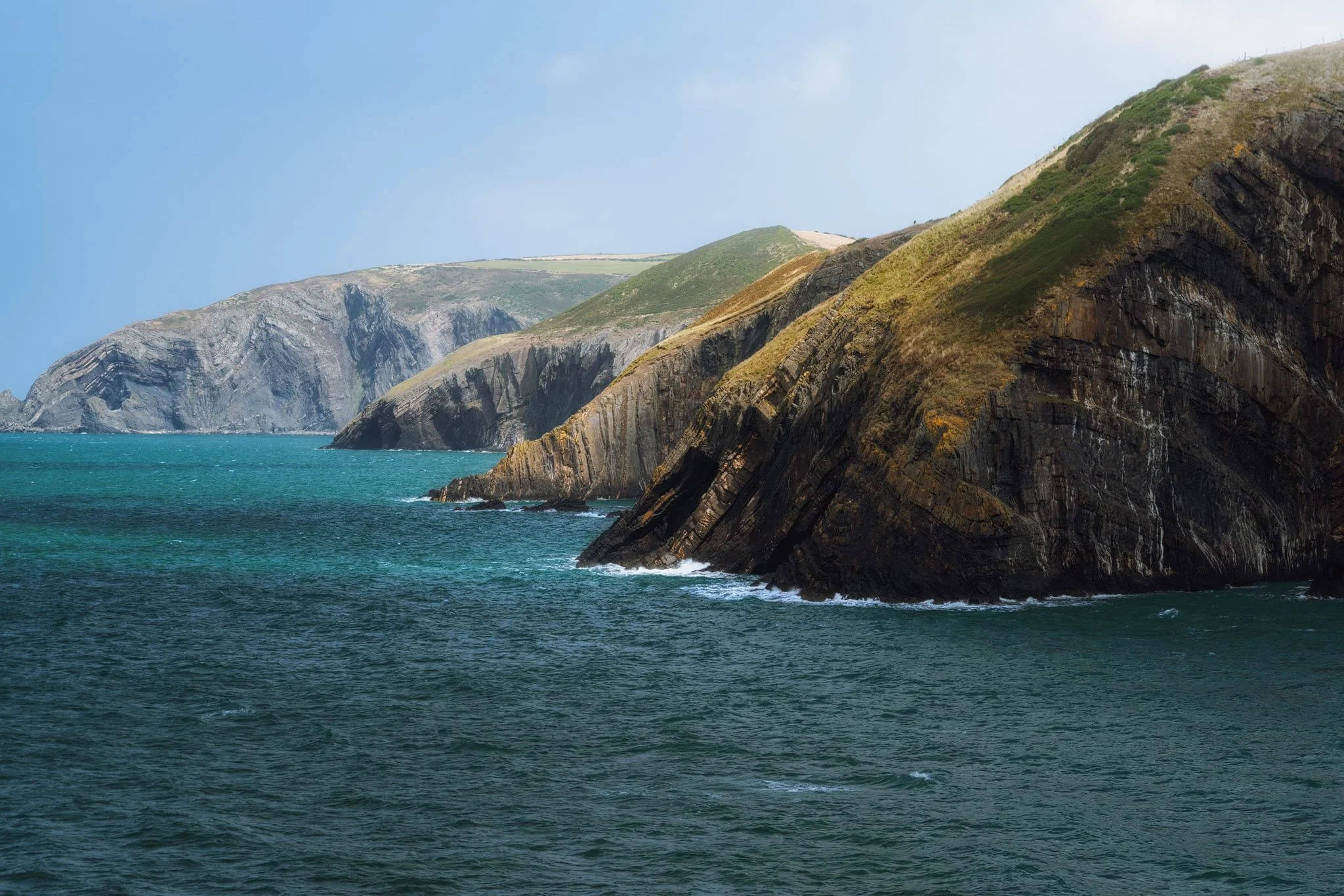  Up on the cliff tops, extensive views north east reveal the cliffs towards  Pen-yr-Afr  and their spectacular synclines and anticlines. 50 million years or so, during the Caledonian Orogeny, colliding continents closed up an ocean basin and crumpled the sedimentary strata, giving rise to these impressive  anticlines (upland ridges) and synclines (valleys and lowlands). 