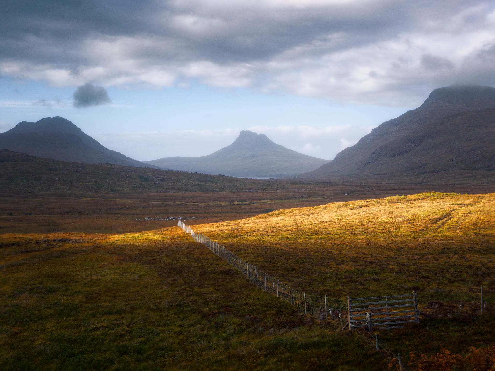South of Knockan Crag, we stopped for more compositions at the Coigach Geopod. A gap in the racing clouds let slithers of golden light race across the landscape. I positioned my composition using the fencing as a leading line and waited for the light to best pick out the lay of the land. Stac Pollaidh once again sits in the middle, but this time its compositional neighbours are Cùl Beag on the right and Beinn Tarsuinn on the left, itself part of the Ben More Coigach ridge.