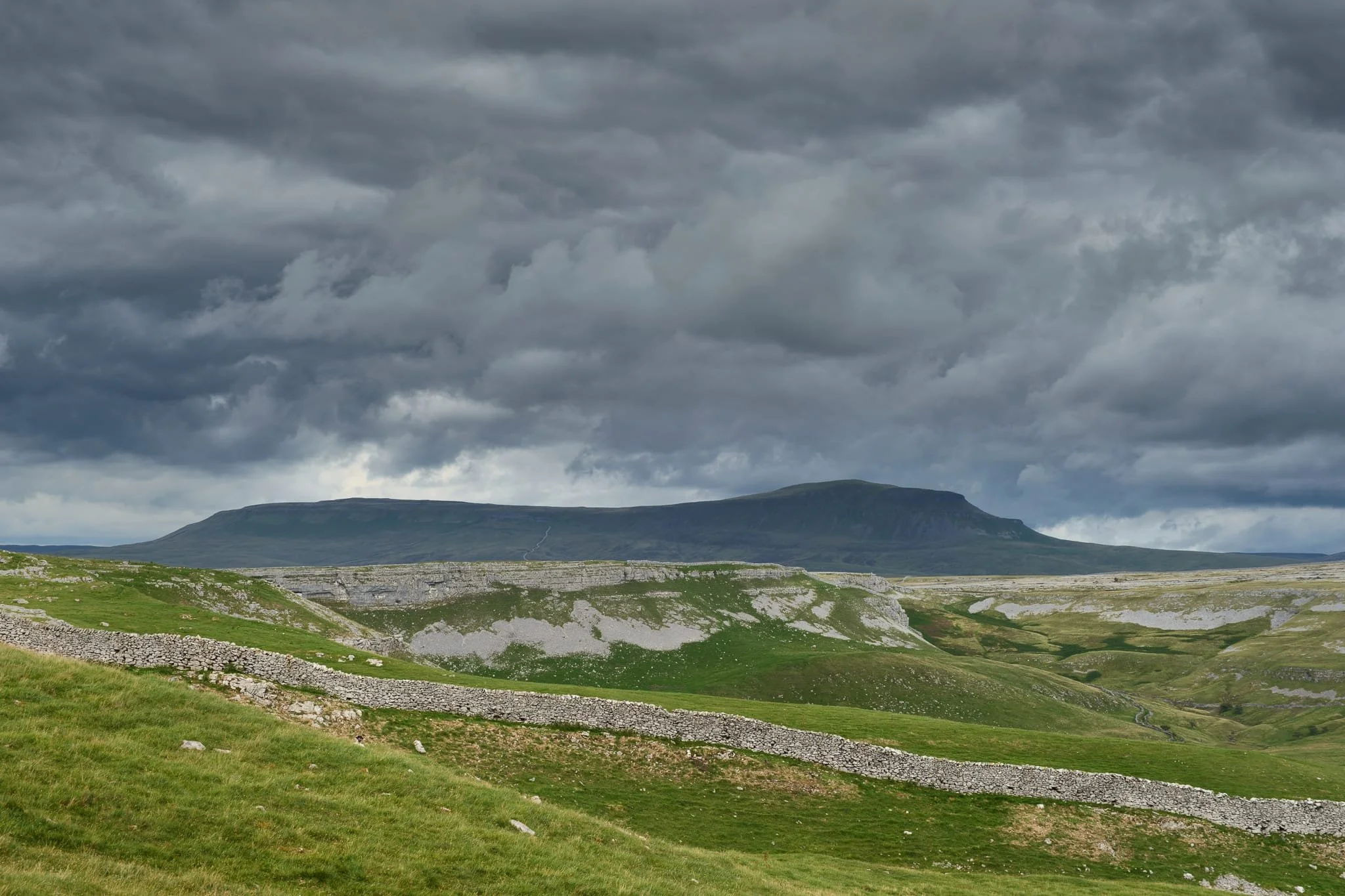  Once we ascended the valley side and up onto the Pennine Bridleway, the dark and foreboding shape of Pen-y-Ghent made its presence very much known to us. Wow. Dark and stormy clouds set the fell in deep shadow, whilst the scars of Crummackdale were lit up by the breaking sun behind us. 
