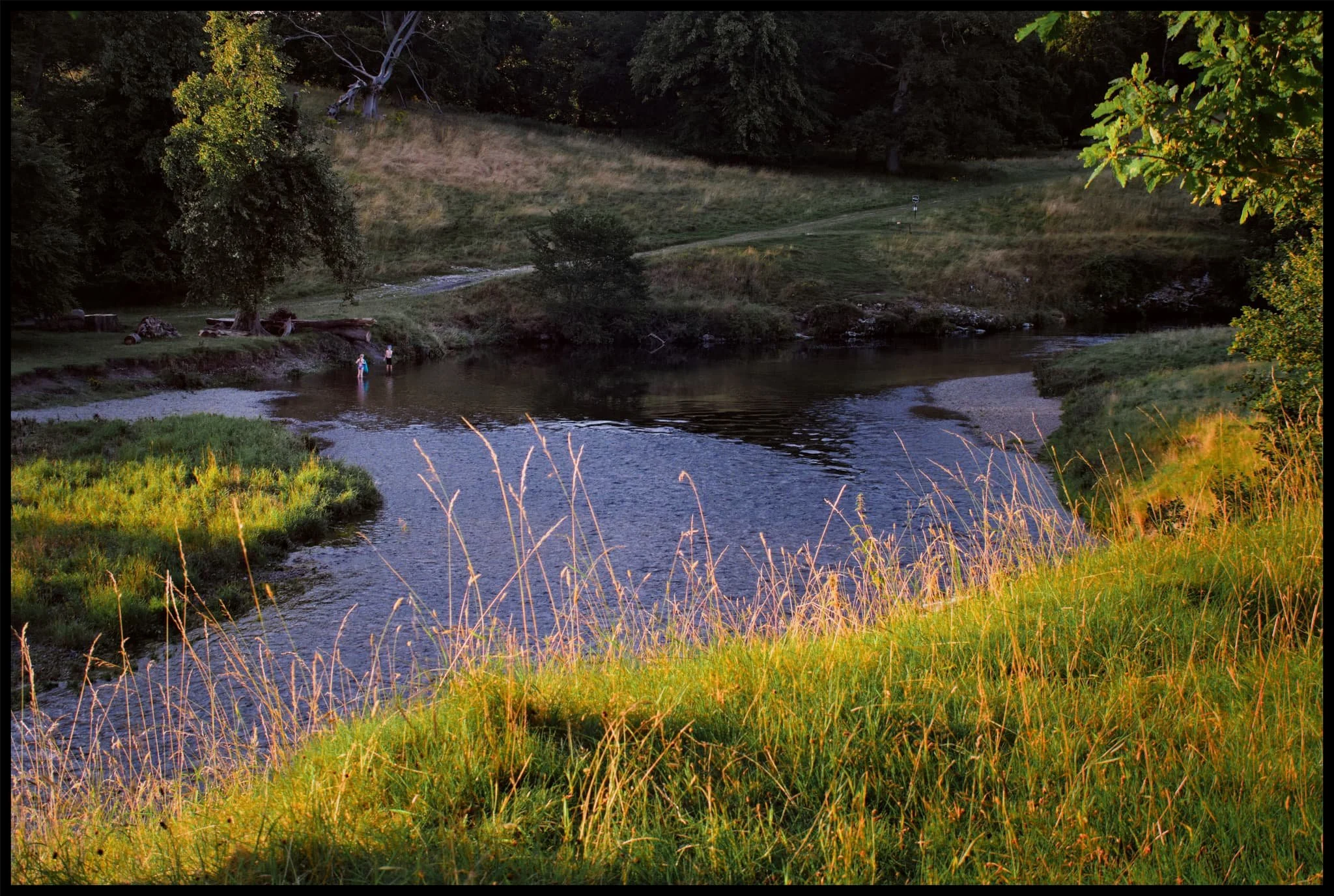  Siblings have fun playing in the river as the low summer sunset catches the glowing grass. 