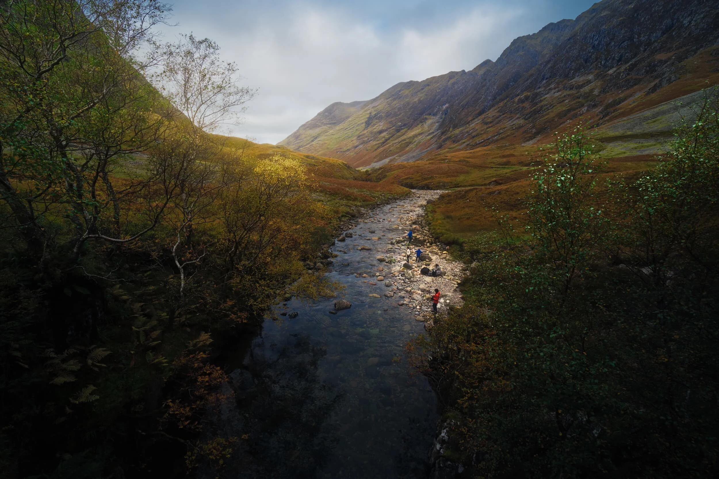  A family play by the calm waters of the River Coe. The giant 10 km ridge in the distance is  Aonach Eagach , which rises to 967 m/3,175 ft and borders the northern side of the valley. 