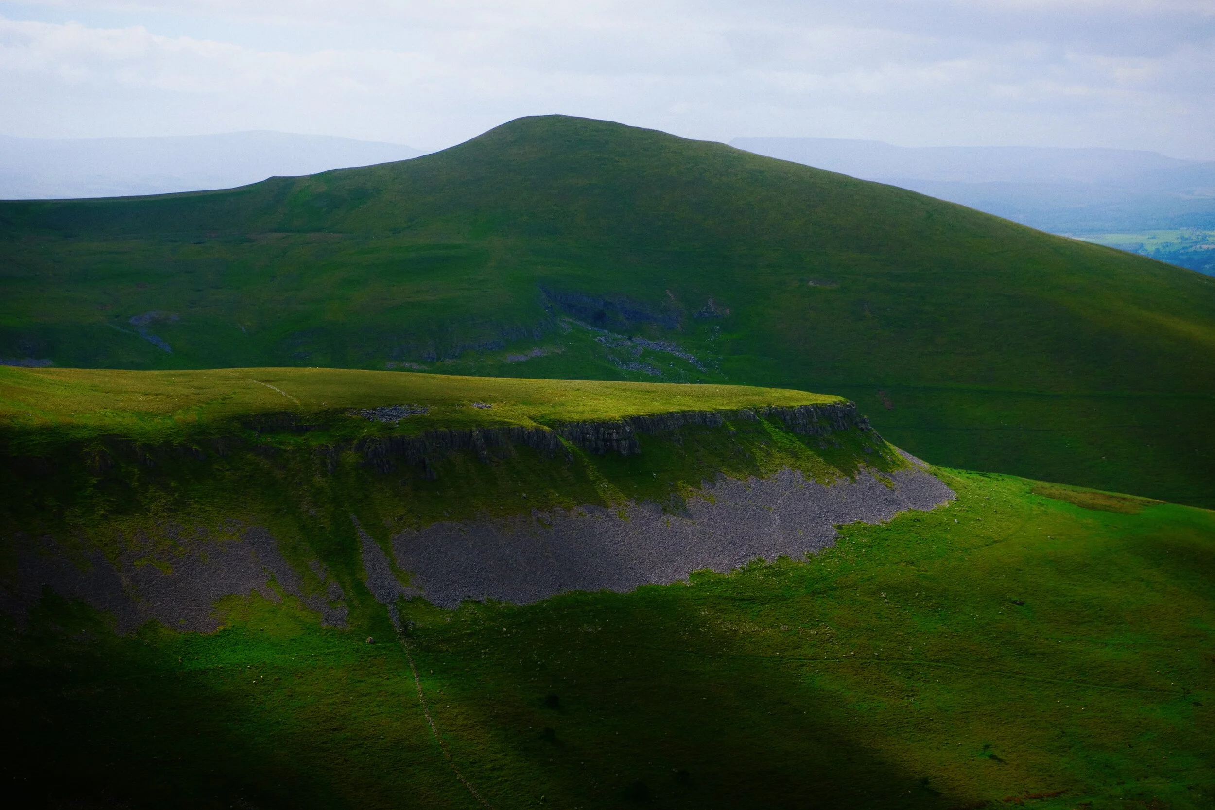  As we round the shoulder of Peeping Hill (510 m/1,673 ft) a look southeast reveals the flat-topped Middletongue Crag (456 m/1,496 ft) being highlighted, with Murton Pike&rsquo;s (594 m/1,949 ft) gentle slopes looming above. 