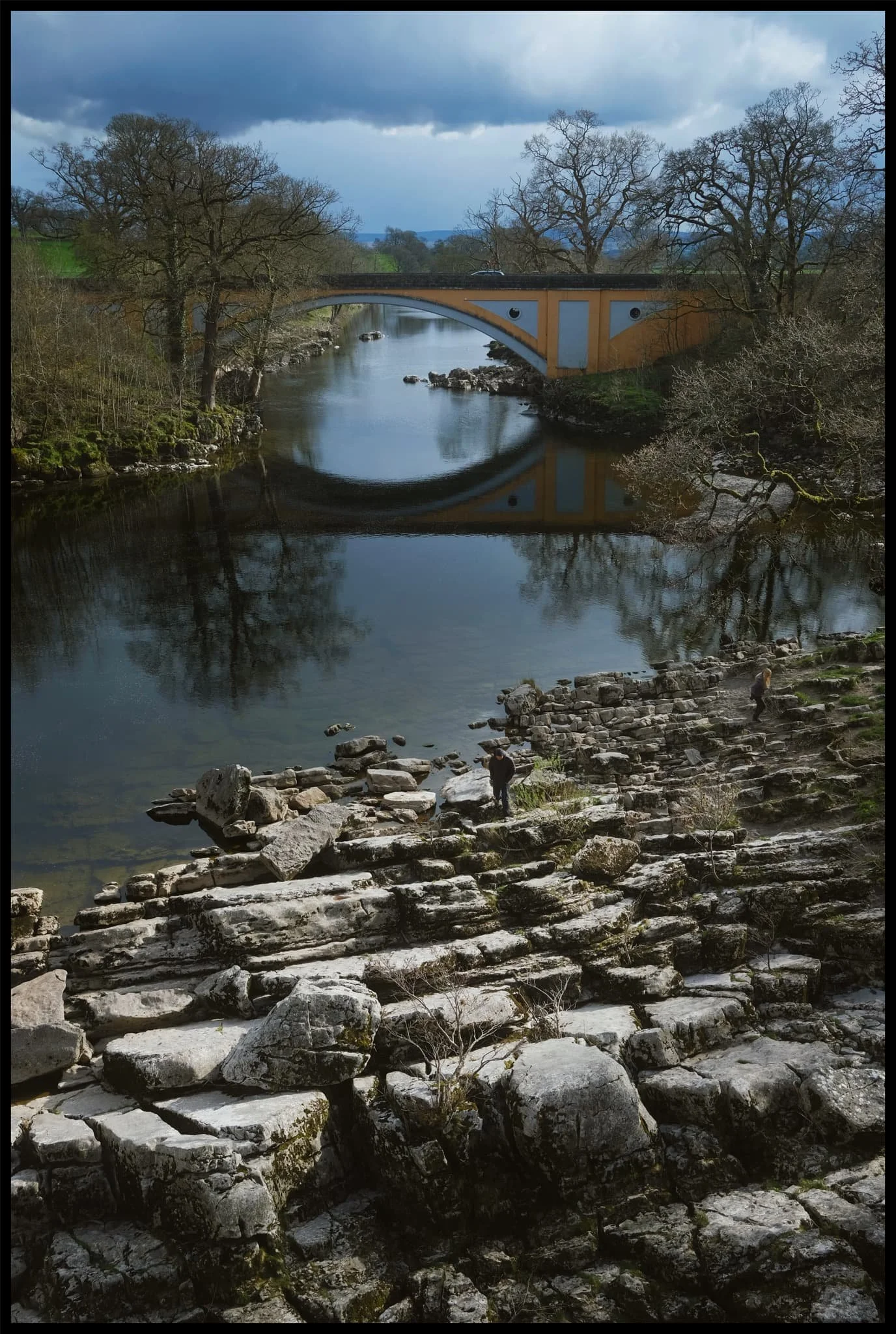  On top of Devil&rsquo;s Bridge a clear is offered to Stanley Bridge, which carries the A65 over the River Lune. Below, some folk play around the limestone formations alongside the river. 