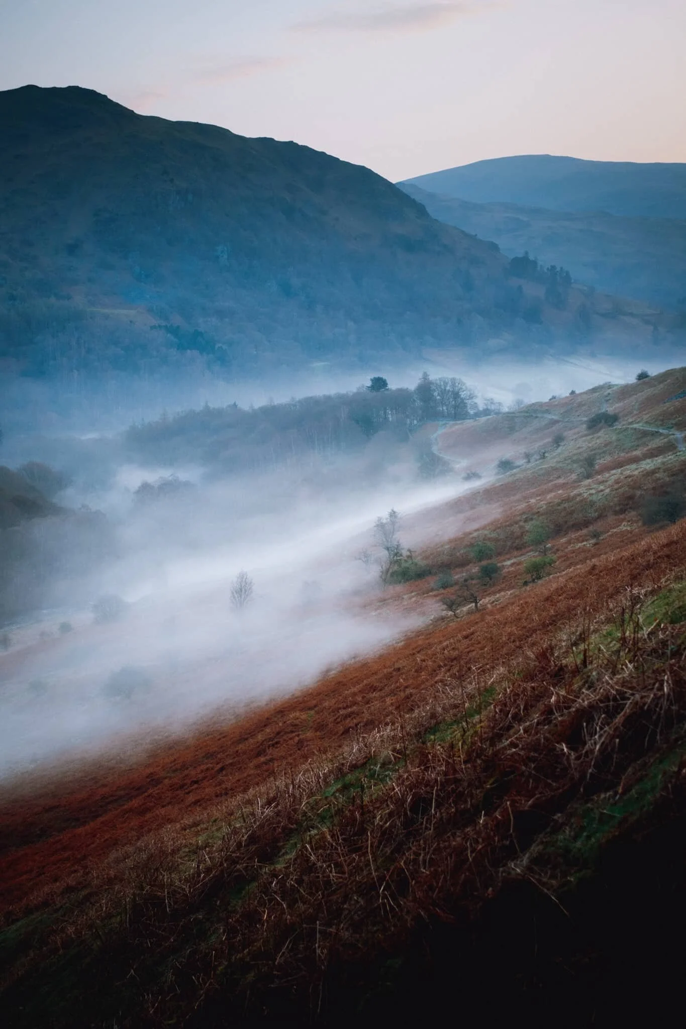  As we began ascending the main footpath up Loughrigg Fell the views quickly opened up. From Loughrigg Terrace the temperature inversion was more visible, and I couldn&rsquo;t resist this composition of the mist clinging to the valley, with Nab Scar (455 m/1,493 ft) looming above.  