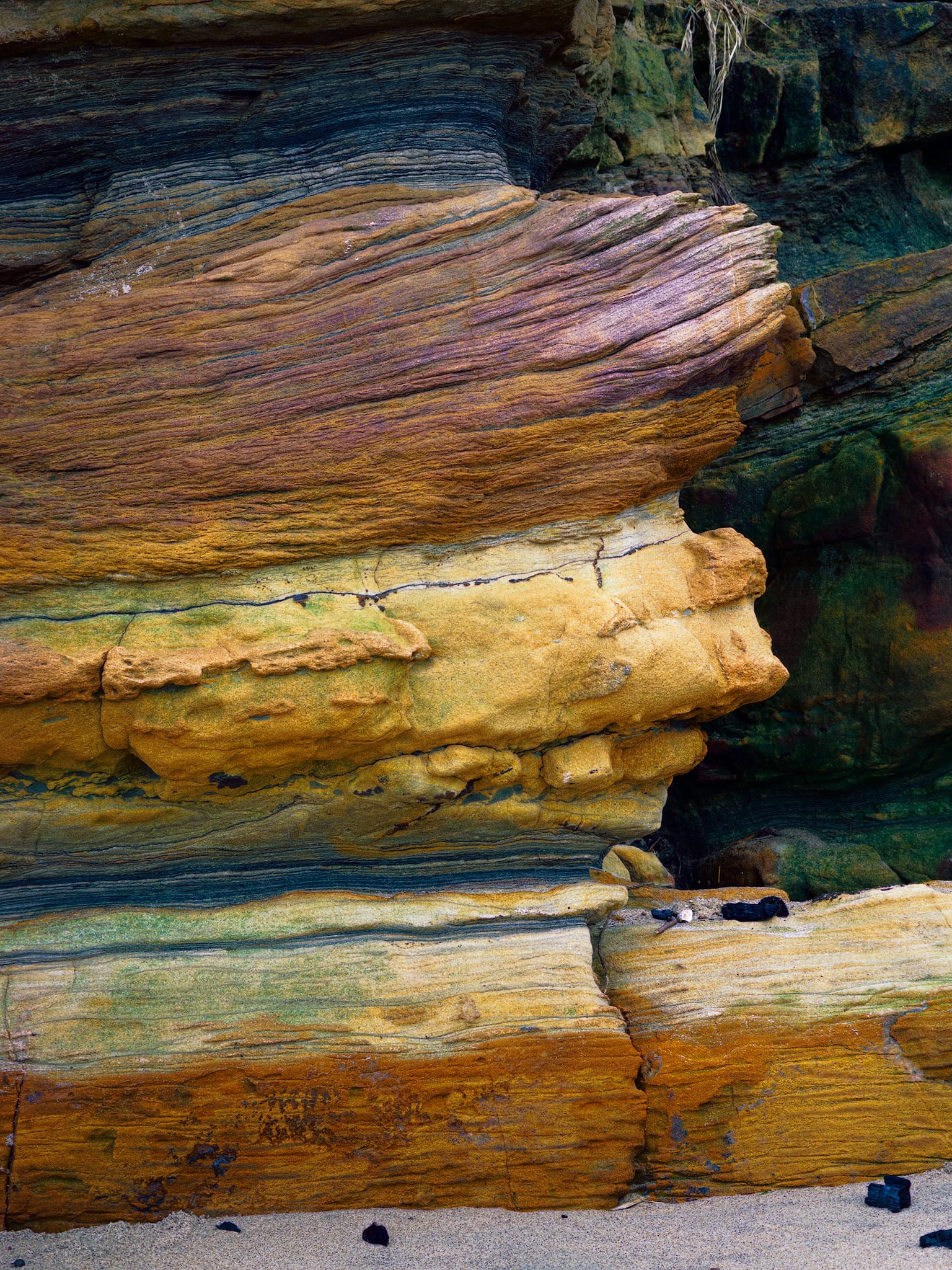 A sandwich of millions of years of history. Red beds bleached to cream, ochre, and gold by shifting groundwater chemistry, these Carboniferous cliff strata are 300 million years of delta cycles laid bare by the sea’s relentless undermining of the softer beds below.